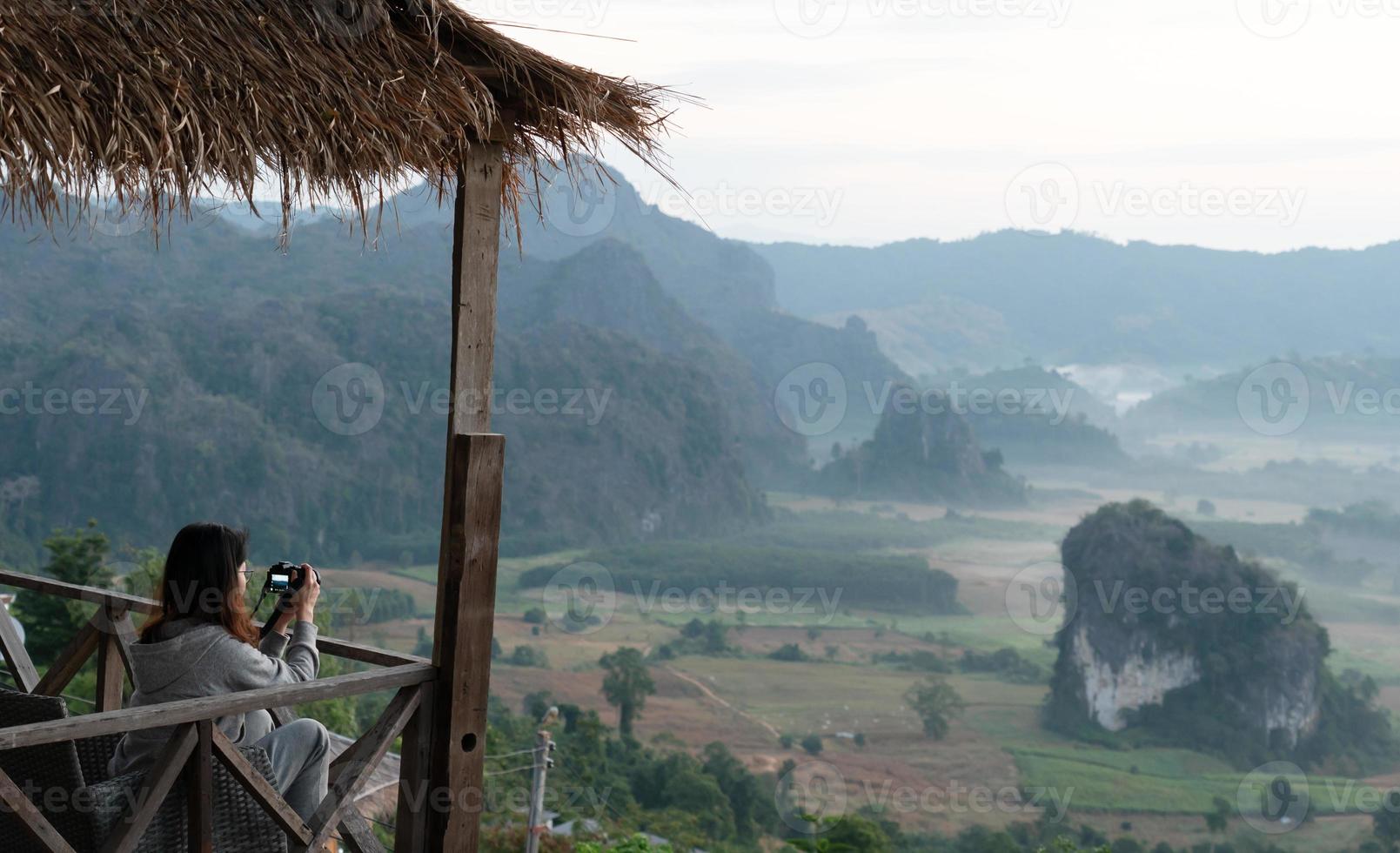 giovane donna asiatica che si sente rilassata e scatta una foto della vista del paesaggio della valle e delle montagne al mattino. concetto di viaggio e vacanza