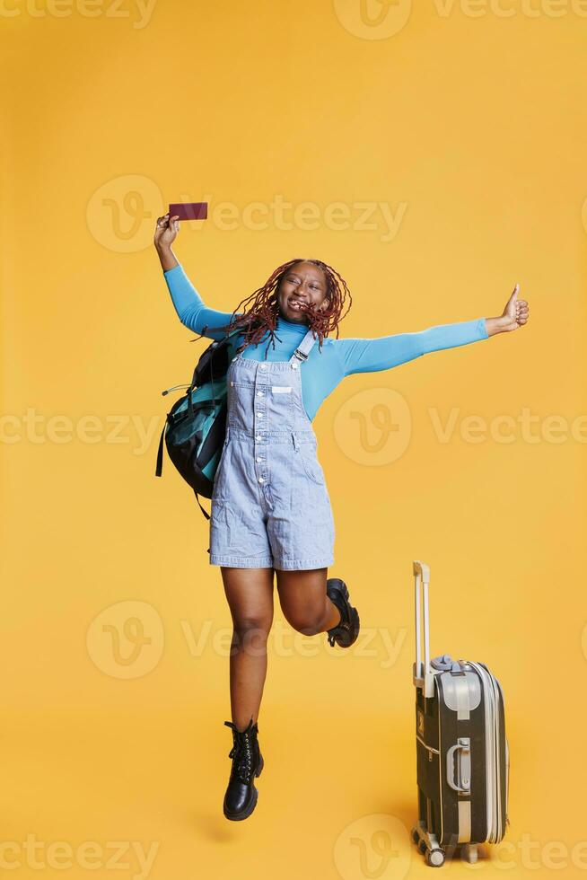 sorridente ragazza salto in giro su telecamera, Tenere id passaggio e trasporto bagaglio borse. giovane donna turista sensazione eccitato di internazionale destinazione, vacanza vacanza con passaporto. foto