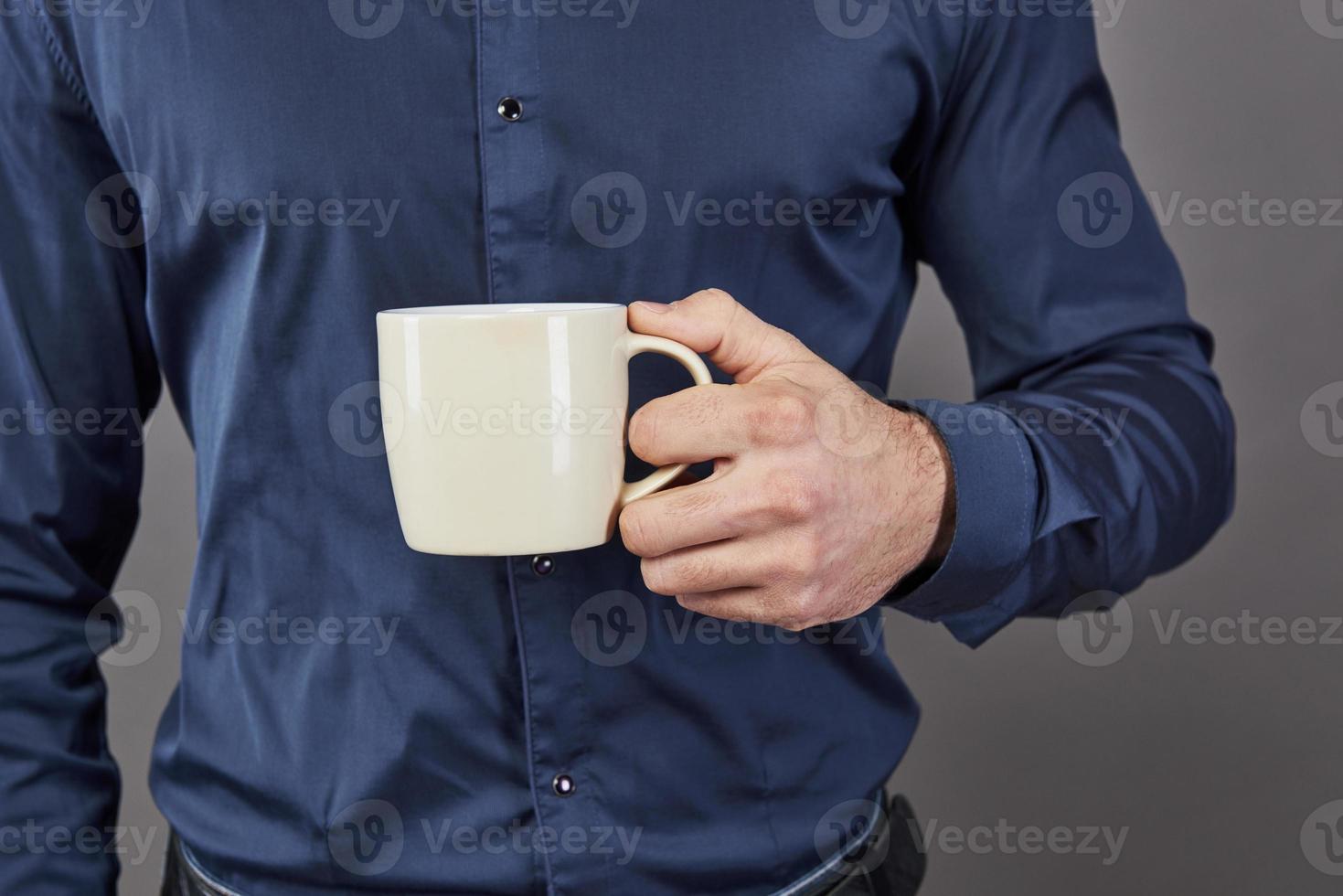 bell'uomo barbuto con capelli alla moda barba e baffi sul viso serio in camicia che tiene tazza bianca o tazza bevendo tè o caffè in studio su sfondo grigio foto