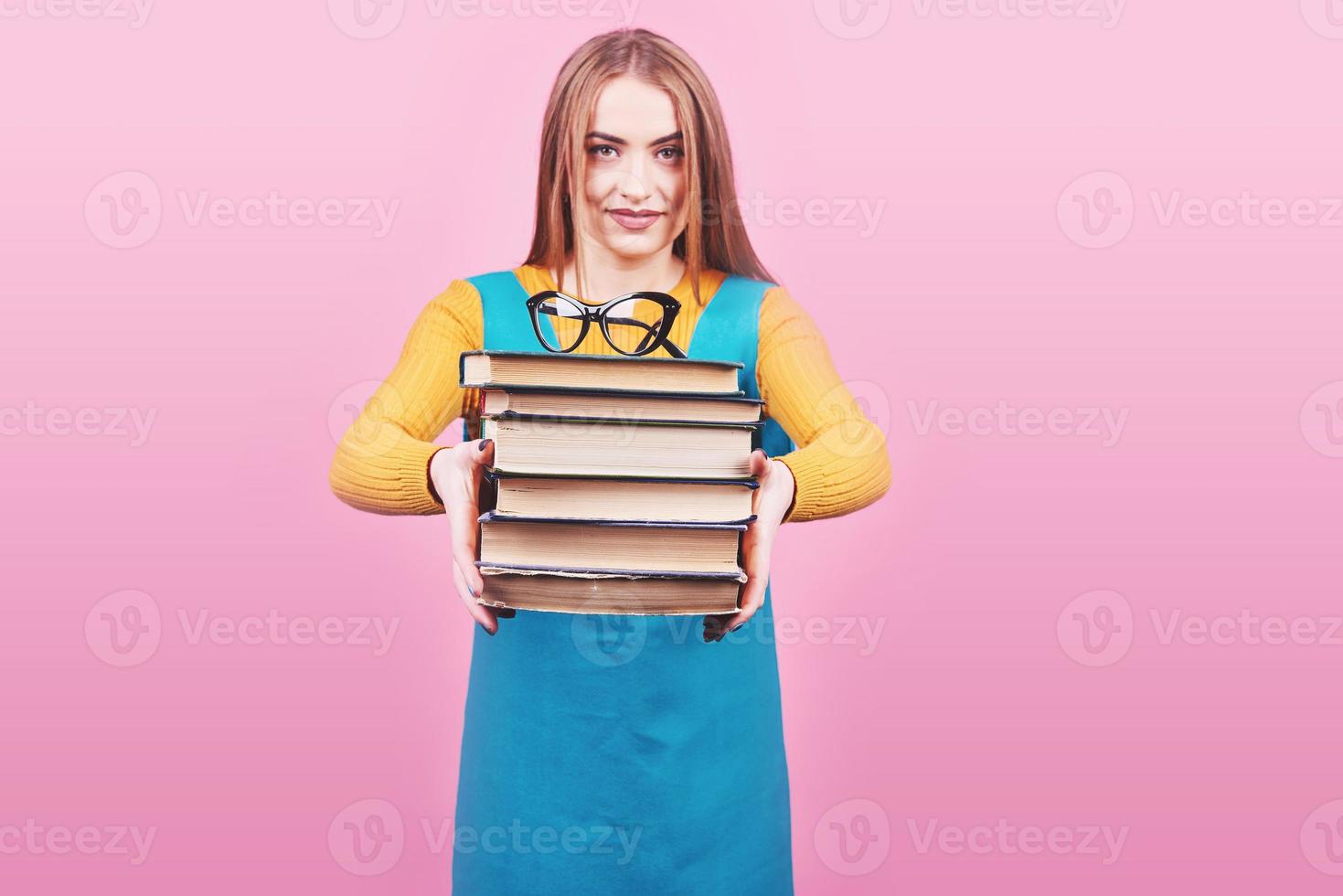 felice ragazza carina che tiene in mano una pila di libri isolati su sfondo rosa colorato. foto