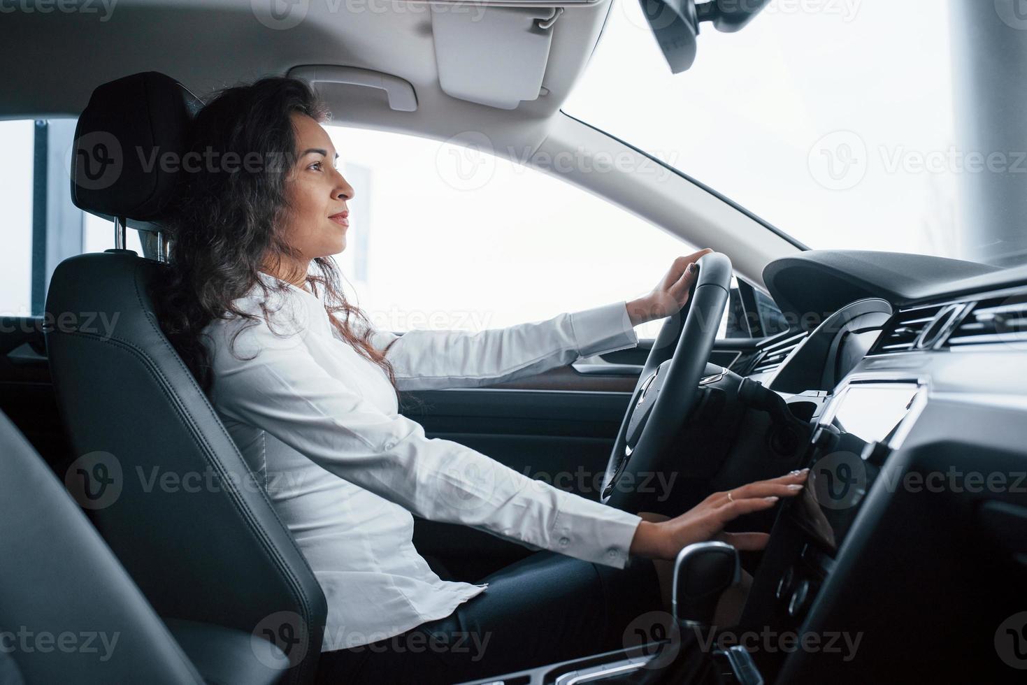 bella donna d'affari che prova la sua nuova auto nel salone dell'automobile foto