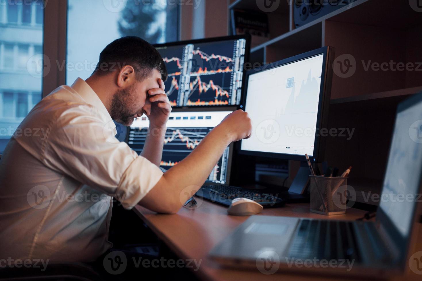 giornata stressante in ufficio. giovane uomo d'affari che si tiene per mano sul viso mentre è seduto alla scrivania in ufficio creativo. concetto grafico di finanza forex trading di borsa foto