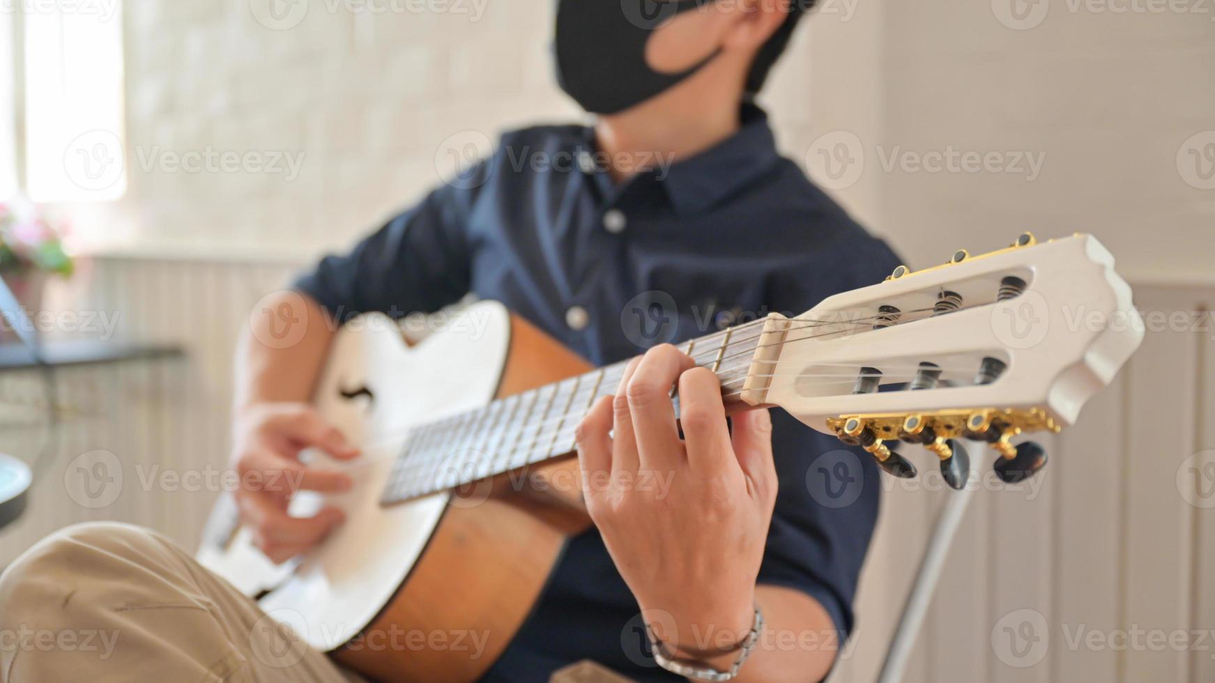 un giovane che indossa una maschera che suona la chitarra a casa, resta a casa, lavora da casa. foto