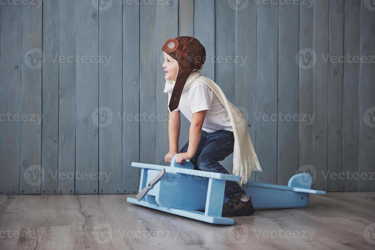 bambino felice in cappello pilota che gioca con l'aeroplano di legno contro. infanzia. fantasia, immaginazione. vacanza foto