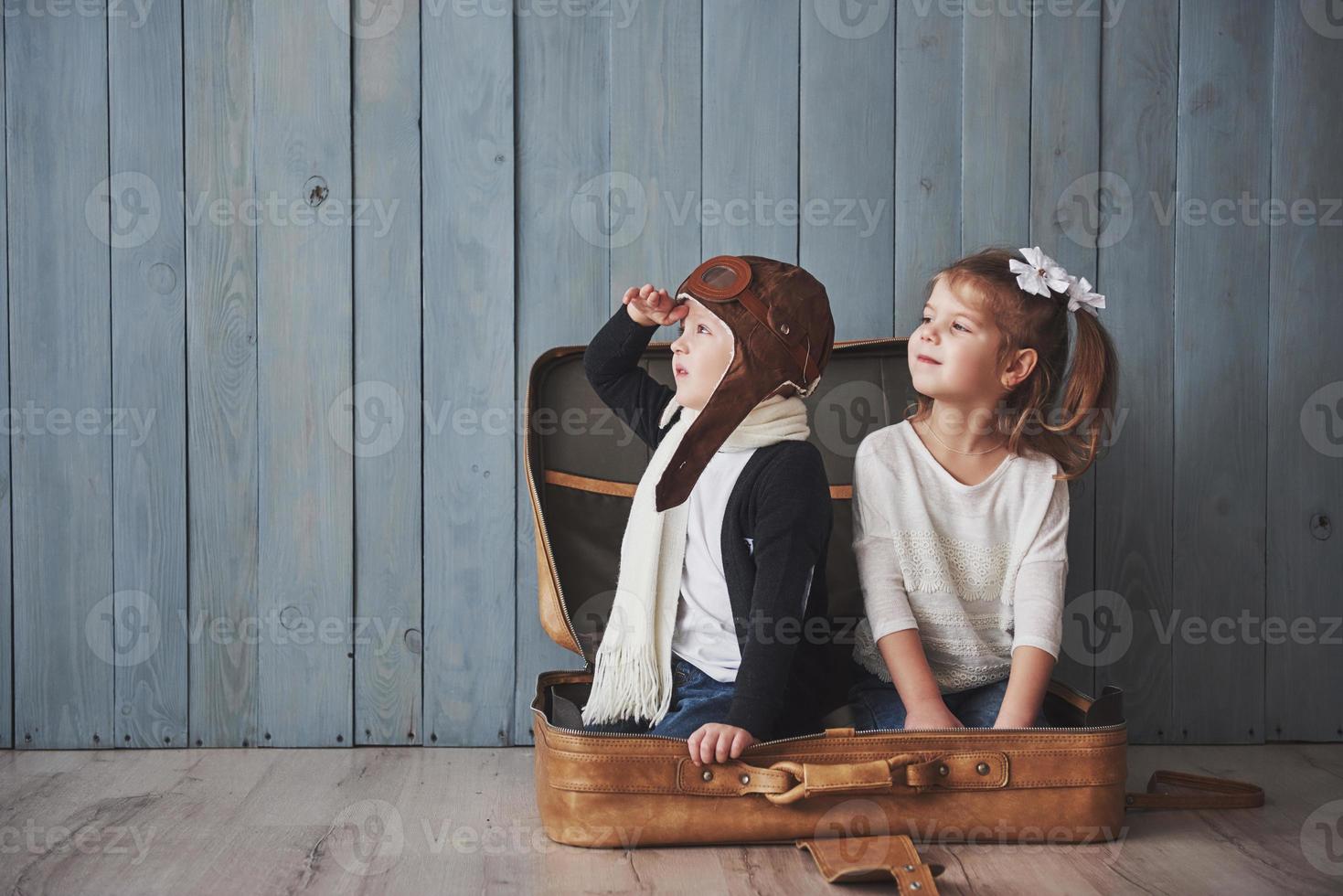 bambino felice in cappello da pilota e bambina che gioca con la vecchia valigia. infanzia. fantasia, immaginazione. concetto di viaggio foto
