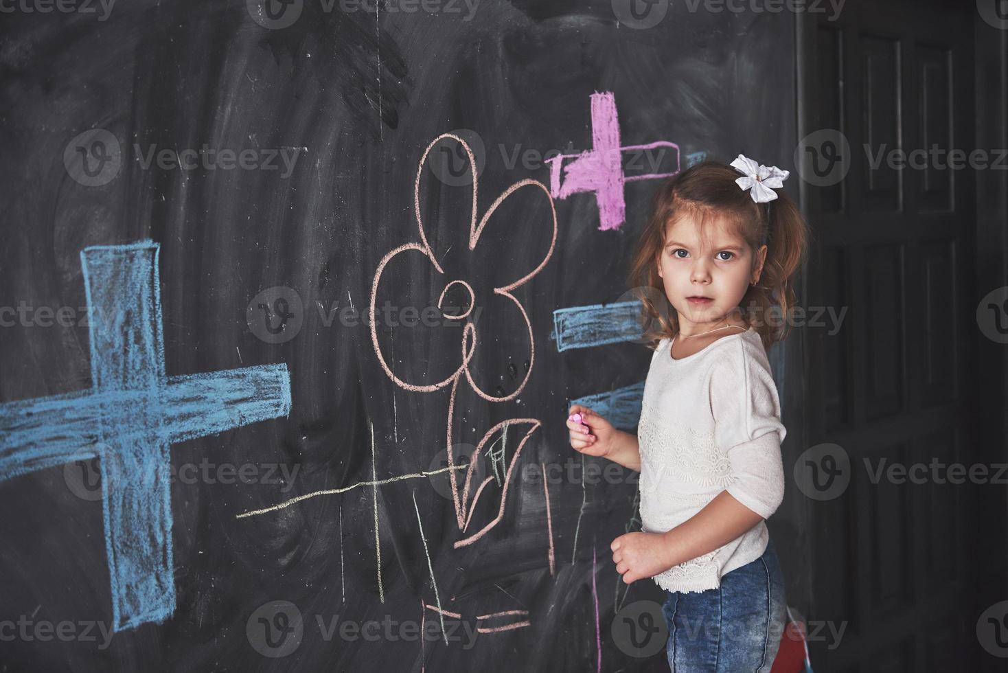 piccola bambina riccia che disegna con i colori a pastello sul muro. opere di bambino. carino allievo che scrive sulla lavagna foto