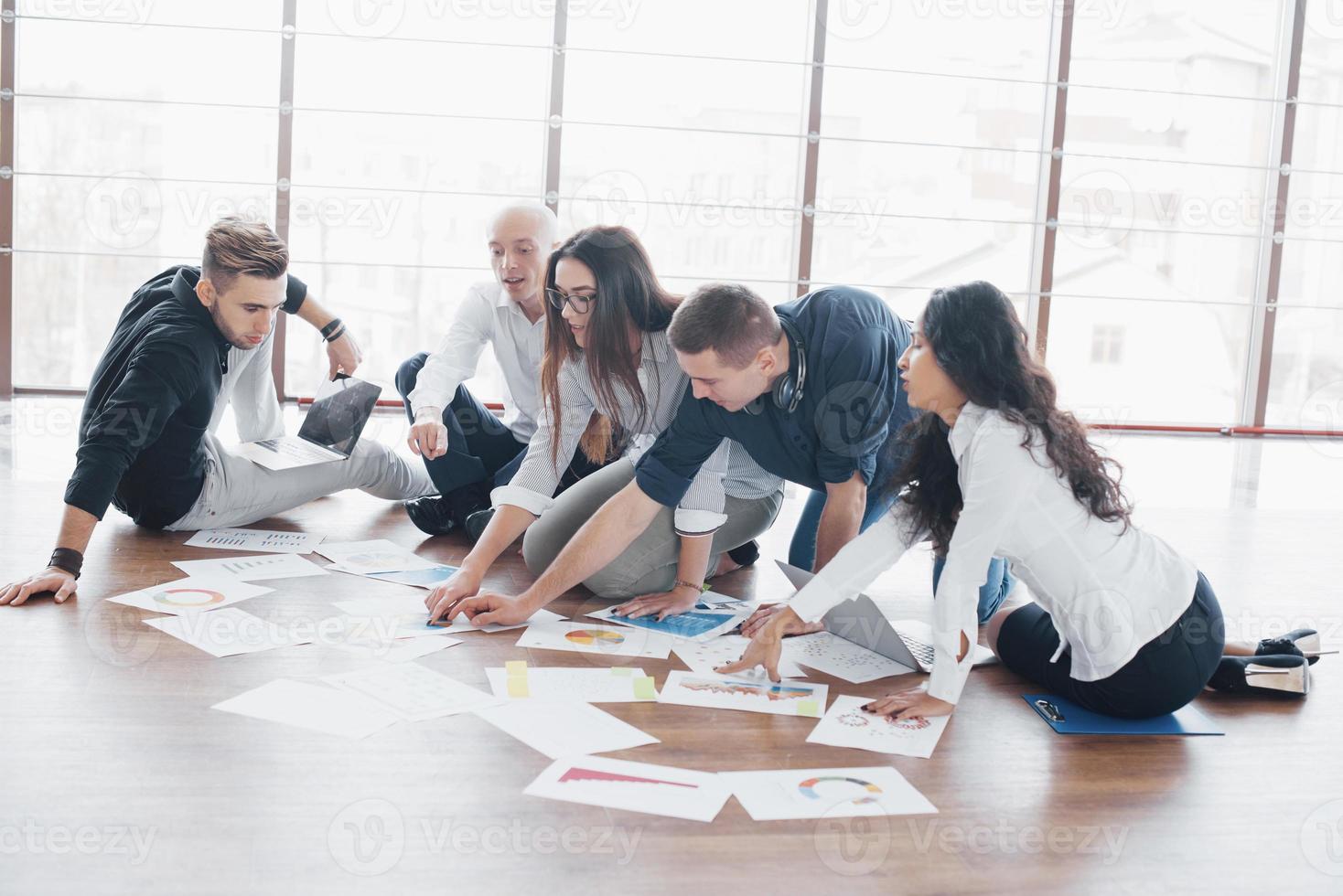 giovani creativi in un ufficio moderno. gruppo di giovani uomini d'affari stanno lavorando insieme al computer portatile. liberi professionisti seduti per terra. cooperazione aziendale successo. concetto di lavoro di squadra foto