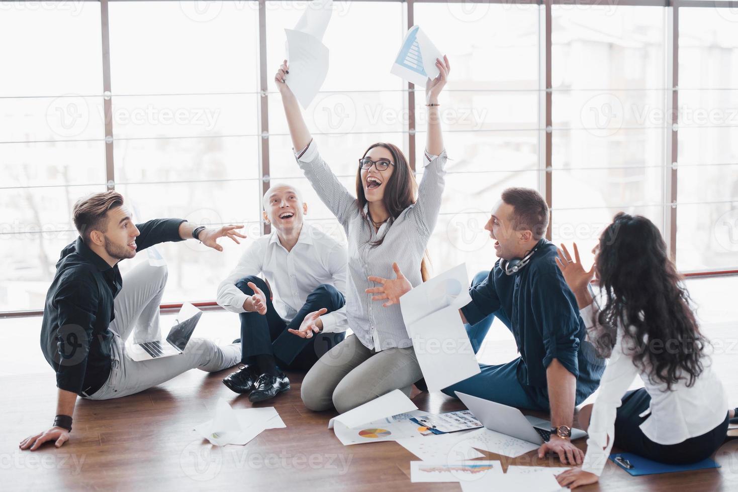 giovani creativi in un ufficio moderno. gruppo di giovani uomini d'affari stanno lavorando insieme al computer portatile. liberi professionisti seduti per terra. cooperazione aziendale successo. concetto di lavoro di squadra foto