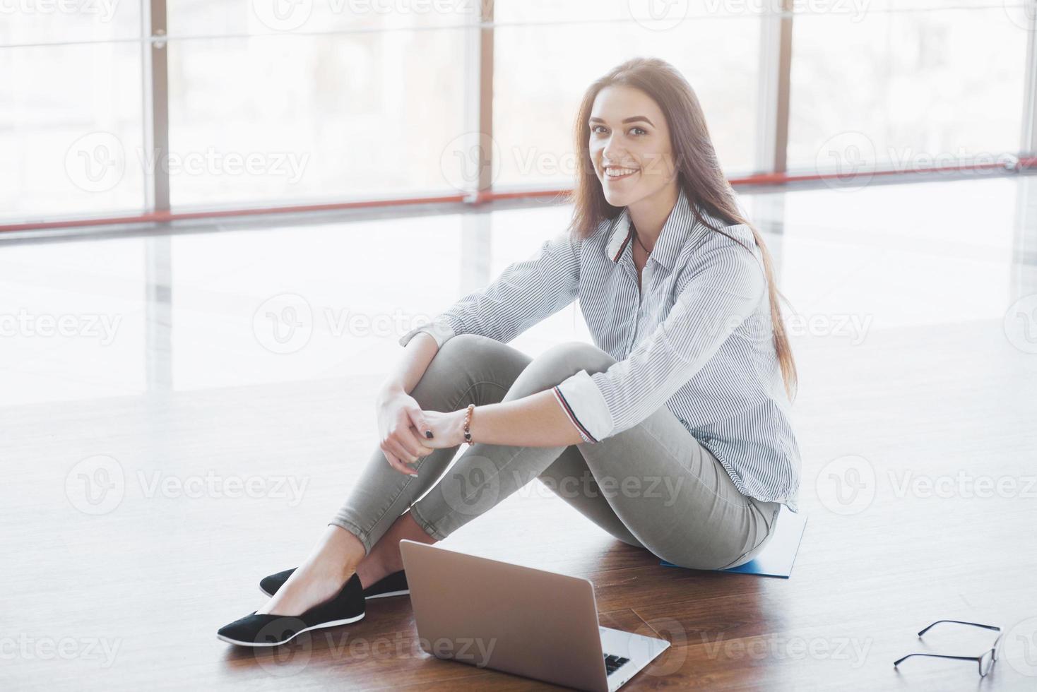 vista laterale di una ragazza attraente che usa un laptop nell'area wifi pubblica e sorride mentre è seduta sul pavimento foto