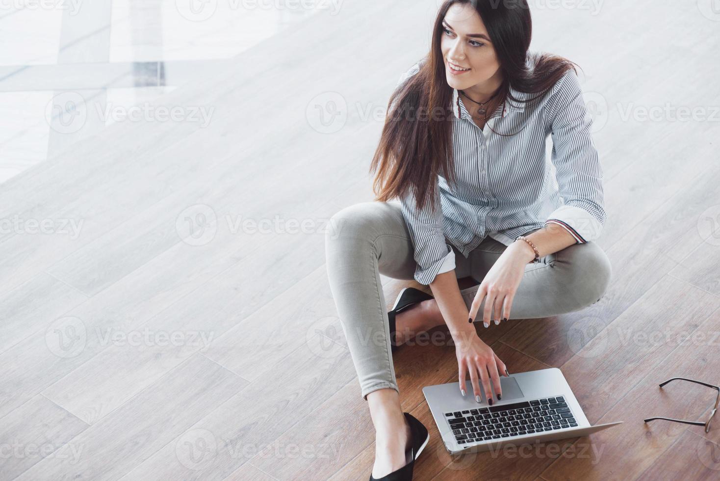 vista laterale di una ragazza attraente che usa un laptop nell'area wifi pubblica e sorride mentre è seduta sul pavimento foto