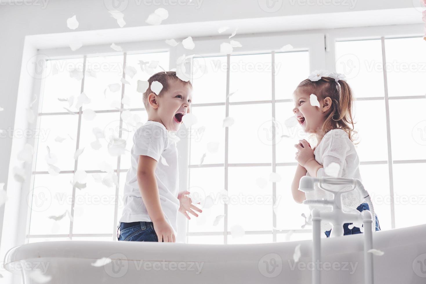 bambino che gioca con petali di rosa nel bagno di casa. bambina e ragazzo fawing divertimento e gioia insieme. il concetto di infanzia e la realizzazione di sogni, fantasia, immaginazione foto