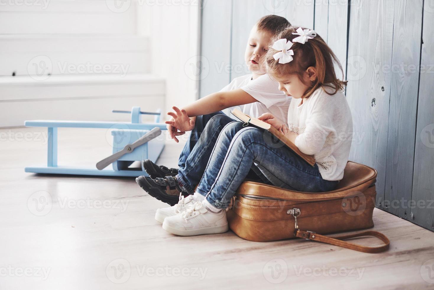 pronto per il grande viaggio. felice bambina e ragazzo che leggono un libro interessante che trasporta una grande valigetta e sorridono. concetto di viaggio, libertà e immaginazione foto