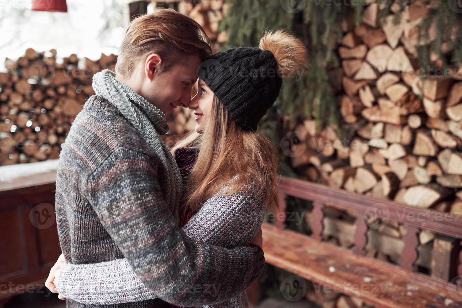 inverno, vacanza, coppia, natale e concetto di persone - uomo e donna sorridenti in cappelli e sciarpa che si abbracciano su una casa di campagna in legno e sullo sfondo della neve foto