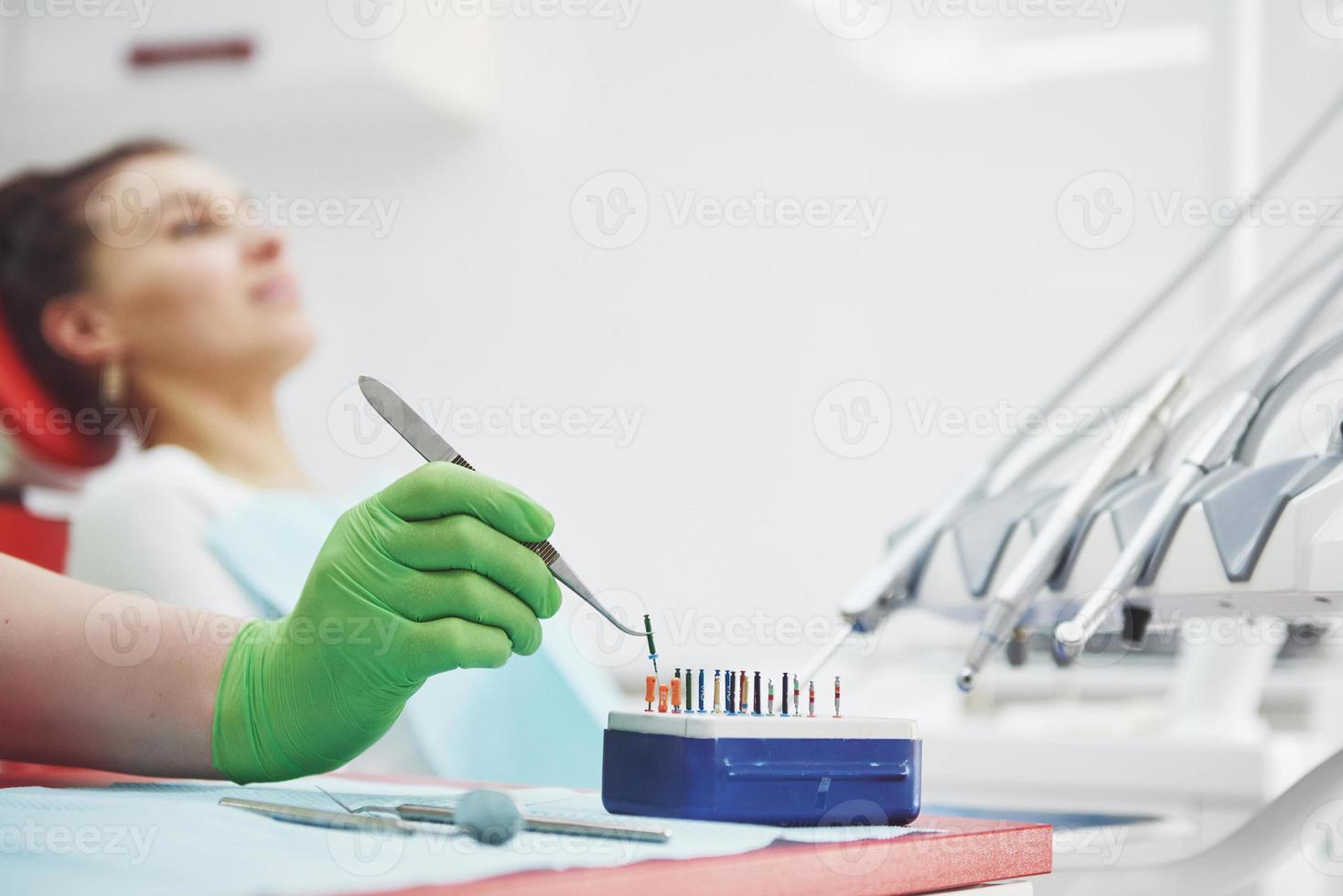 un paziente in una clinica odontoiatrica si siede su una sedia e il medico prepara gli strumenti per il trattamento foto
