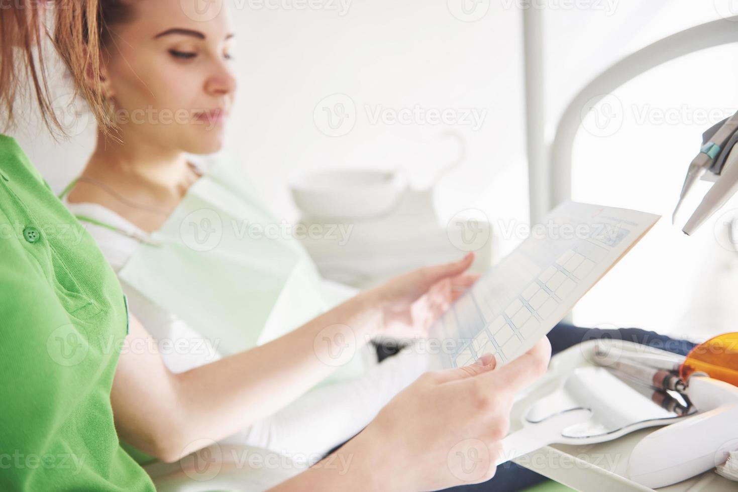 Dentista femminile in studio dentistico che parla con una paziente e si prepara per il trattamento foto