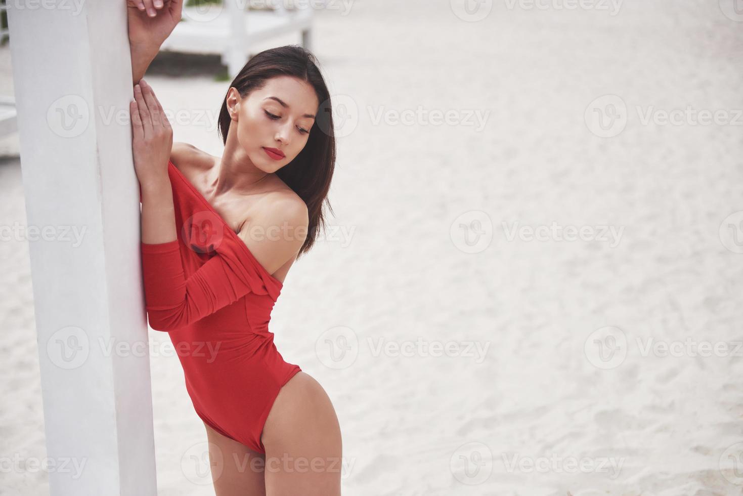 bella giovane donna abbronzata in bikini rosso in posa sulla spiaggia. ritratto modello sexy con un corpo perfetto. concetto di vacanza estiva foto