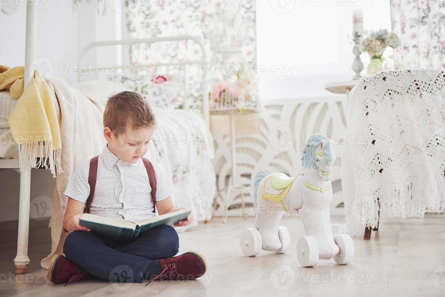 il ragazzino carino sta andando a scuola per la prima volta. bambino con borsa di scuola e libro. il bambino fa una valigetta, la stanza dei bambini su uno sfondo. di nuovo a scuola foto