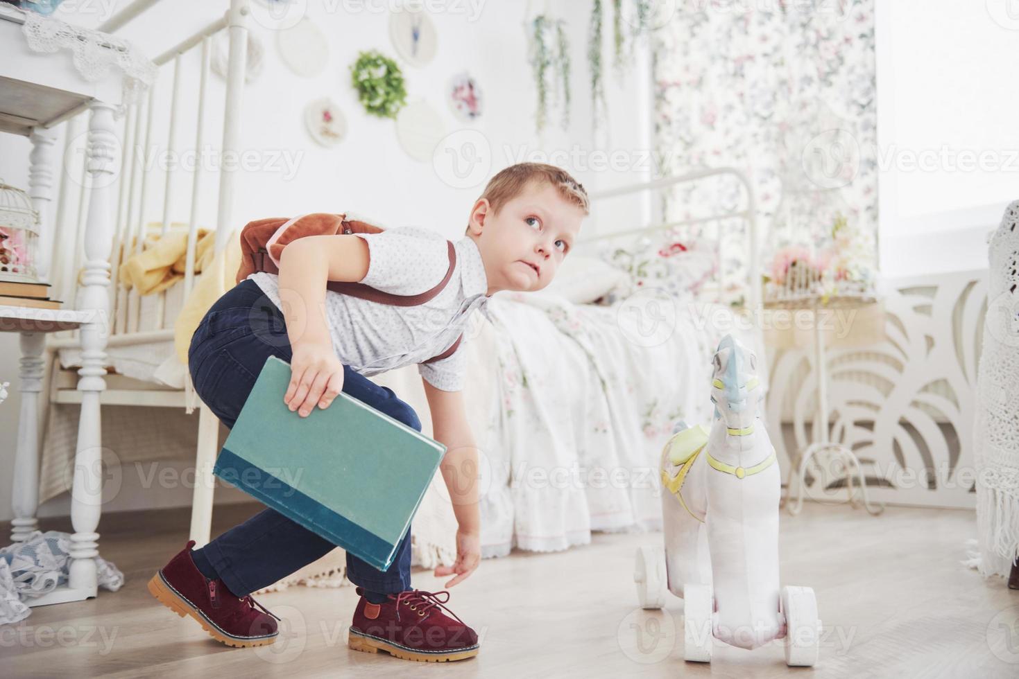 il ragazzino carino sta andando a scuola per la prima volta. bambino con borsa di scuola e libro. il bambino fa una valigetta, la stanza dei bambini su uno sfondo. di nuovo a scuola foto