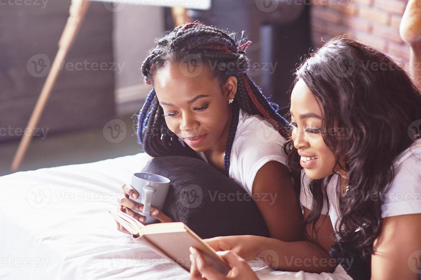 due belle ragazze africane in pigiameria sorridenti sedute sul letto a casa si sono svegliate la mattina in una giornata di sole. foto