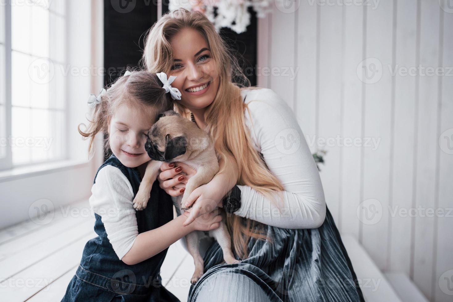 famiglia amorevole felice. madre e figlia bambina che giocano e abbracciano adorabile carlino foto