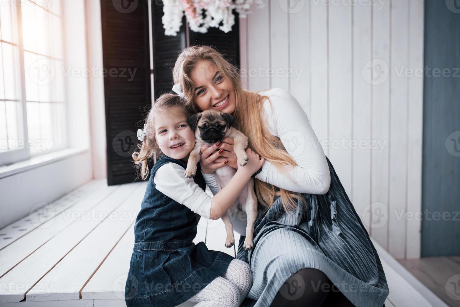 famiglia amorevole felice. madre e figlia bambina che giocano e abbracciano adorabile carlino foto