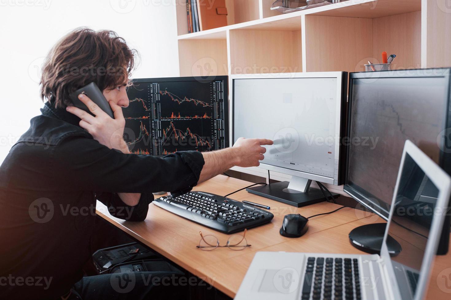 vista da sopra e da un broker di borsa che fa trading online mentre accetta ordini per telefono. più schermi di computer pieni di grafici e analisi dei dati in background foto