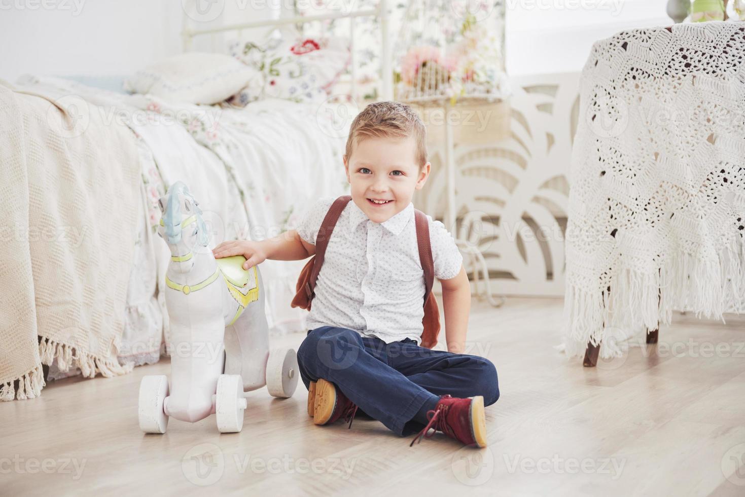 il ragazzino carino sta andando a scuola per la prima volta. bambino con borsa di scuola e libro. il bambino fa una valigetta, la stanza dei bambini su uno sfondo. di nuovo a scuola foto