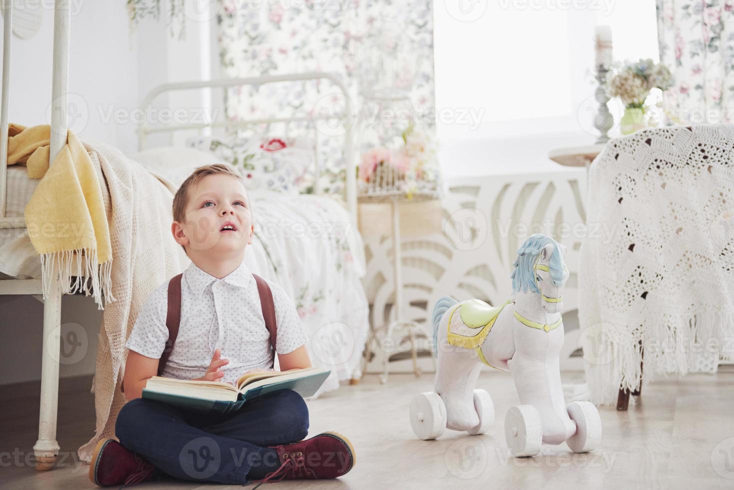 il ragazzino carino sta andando a scuola per la prima volta. bambino con borsa di scuola e libro. il bambino fa una valigetta, la stanza dei bambini su uno sfondo. di nuovo a scuola foto