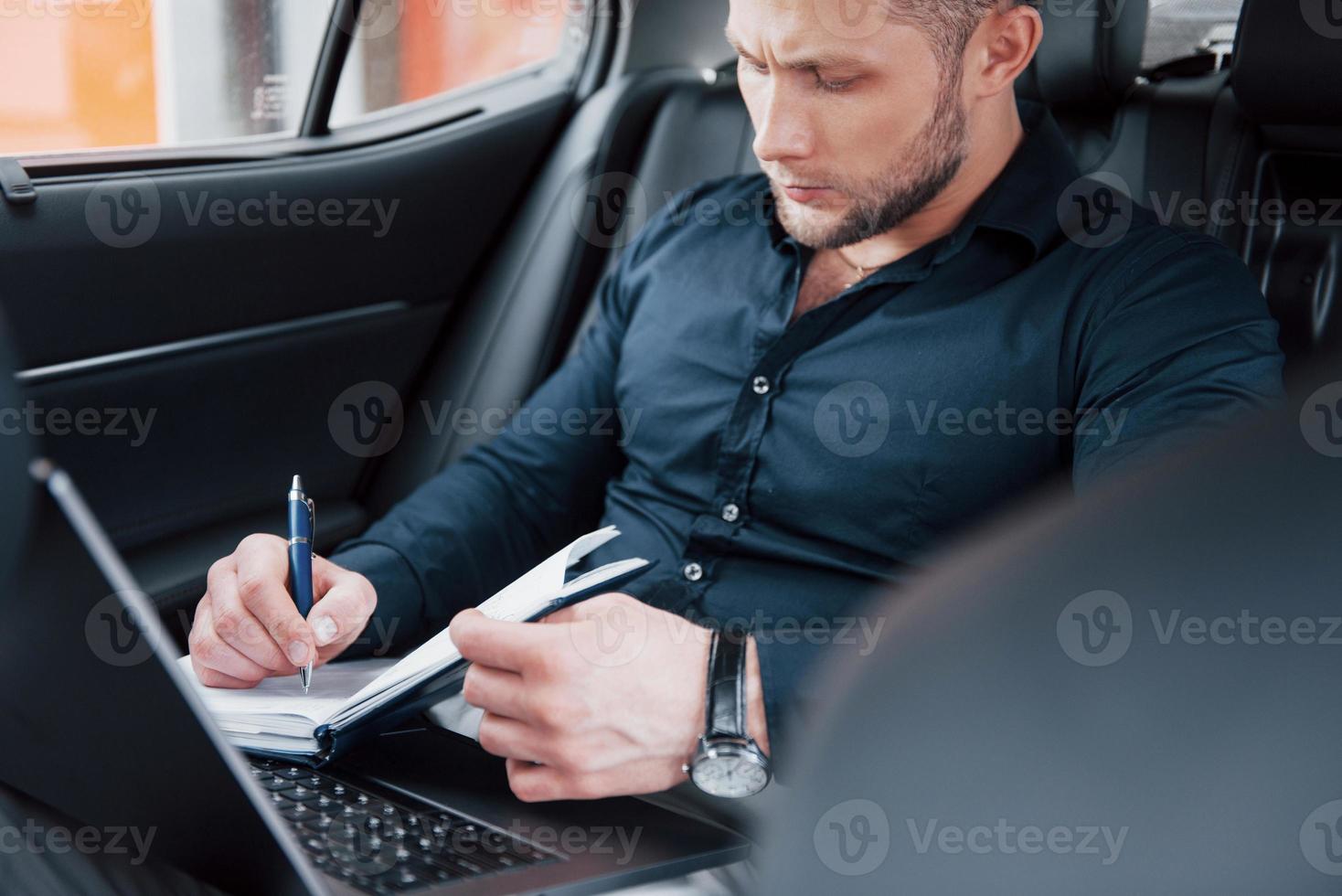 un giovane uomo d'affari sistema i suoi affari con un blocco note mentre è seduto nella parte posteriore dell'auto foto