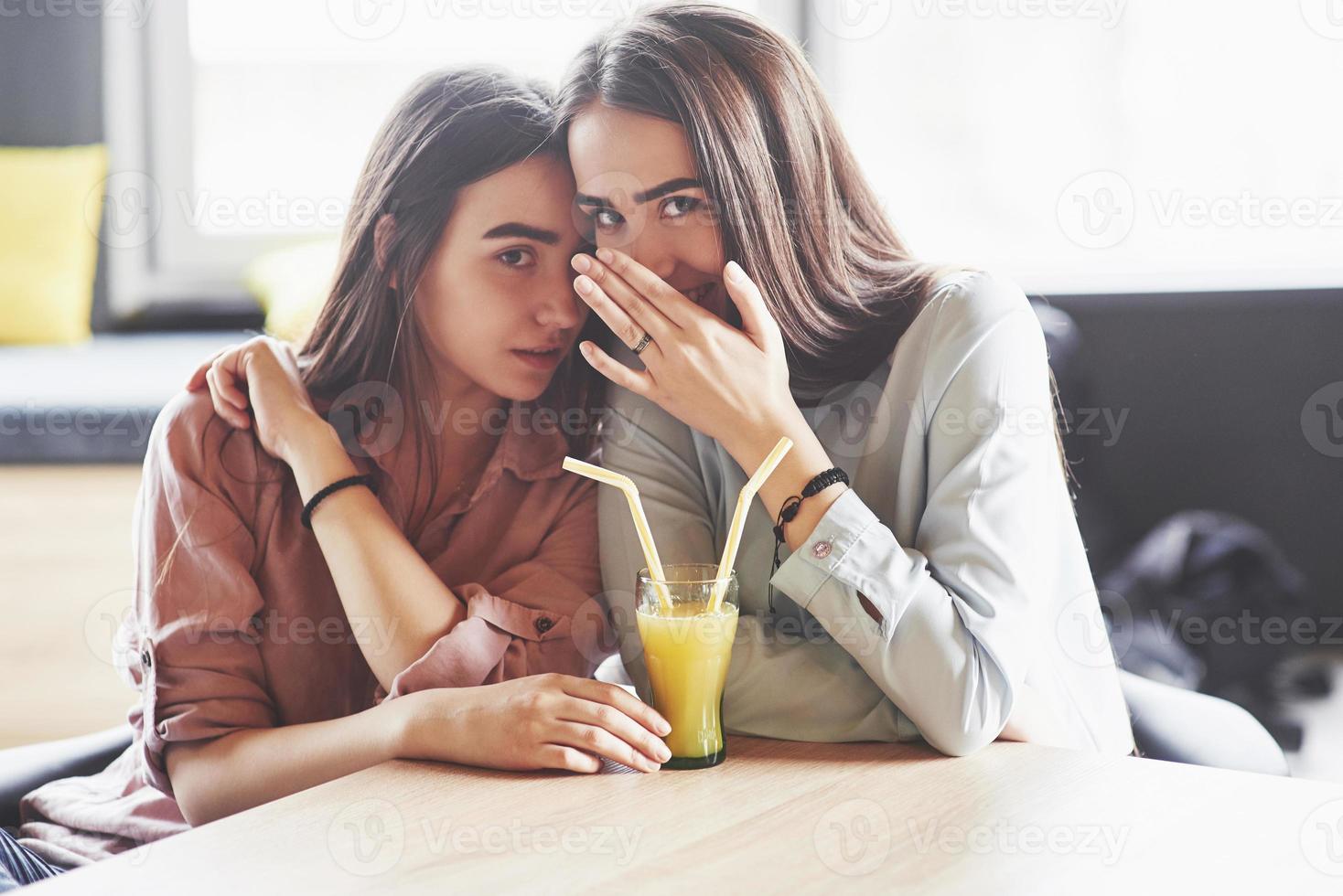 due bellissime gemelle trascorrono del tempo a bere succo di frutta. sorelle che si rilassano in un bar e si divertono insieme e sussurrano foto