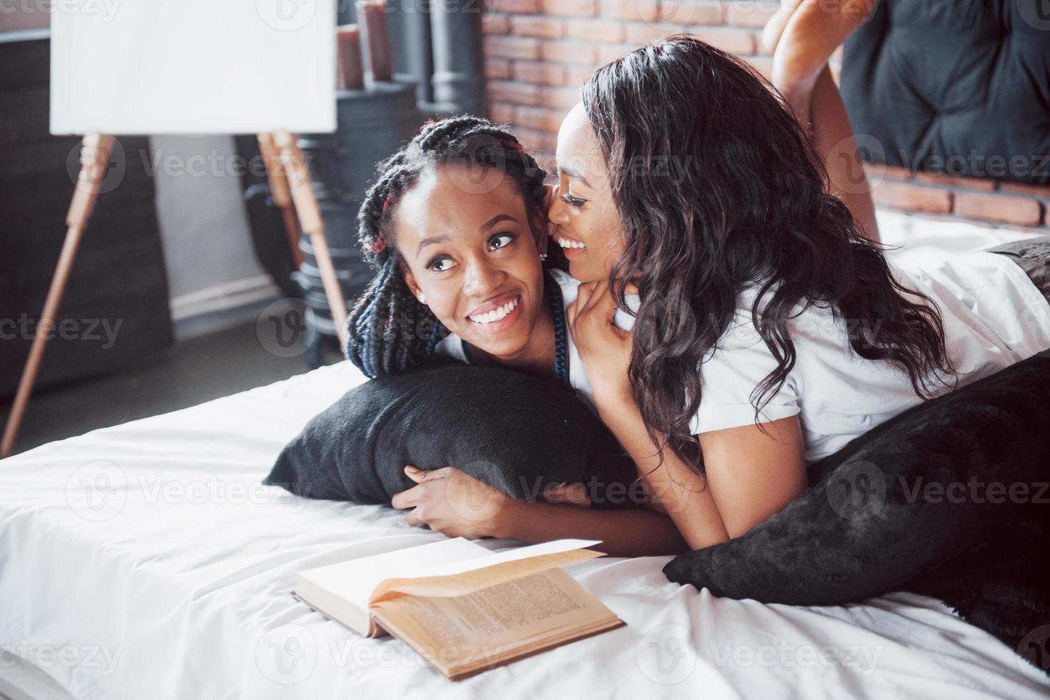 due belle ragazze africane in pigiameria sorridenti sedute sul letto a casa si sono svegliate la mattina in una giornata di sole. foto