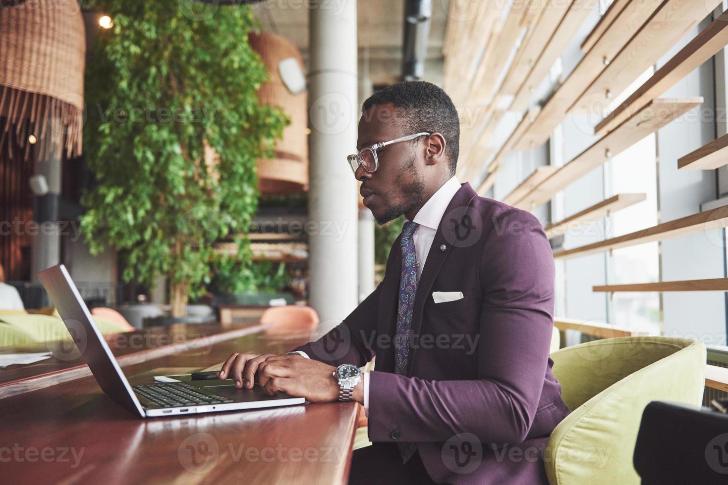 una bella ed elegante donna d'affari afroamericana che indossa un abito usa il suo laptop mentre lavora foto