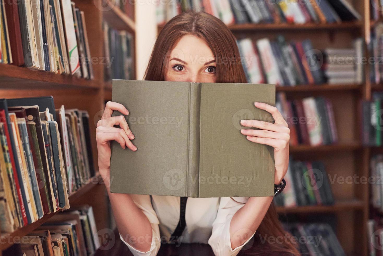 giovane bibliotecario studente attraente che legge un libro tra gli scaffali della biblioteca foto