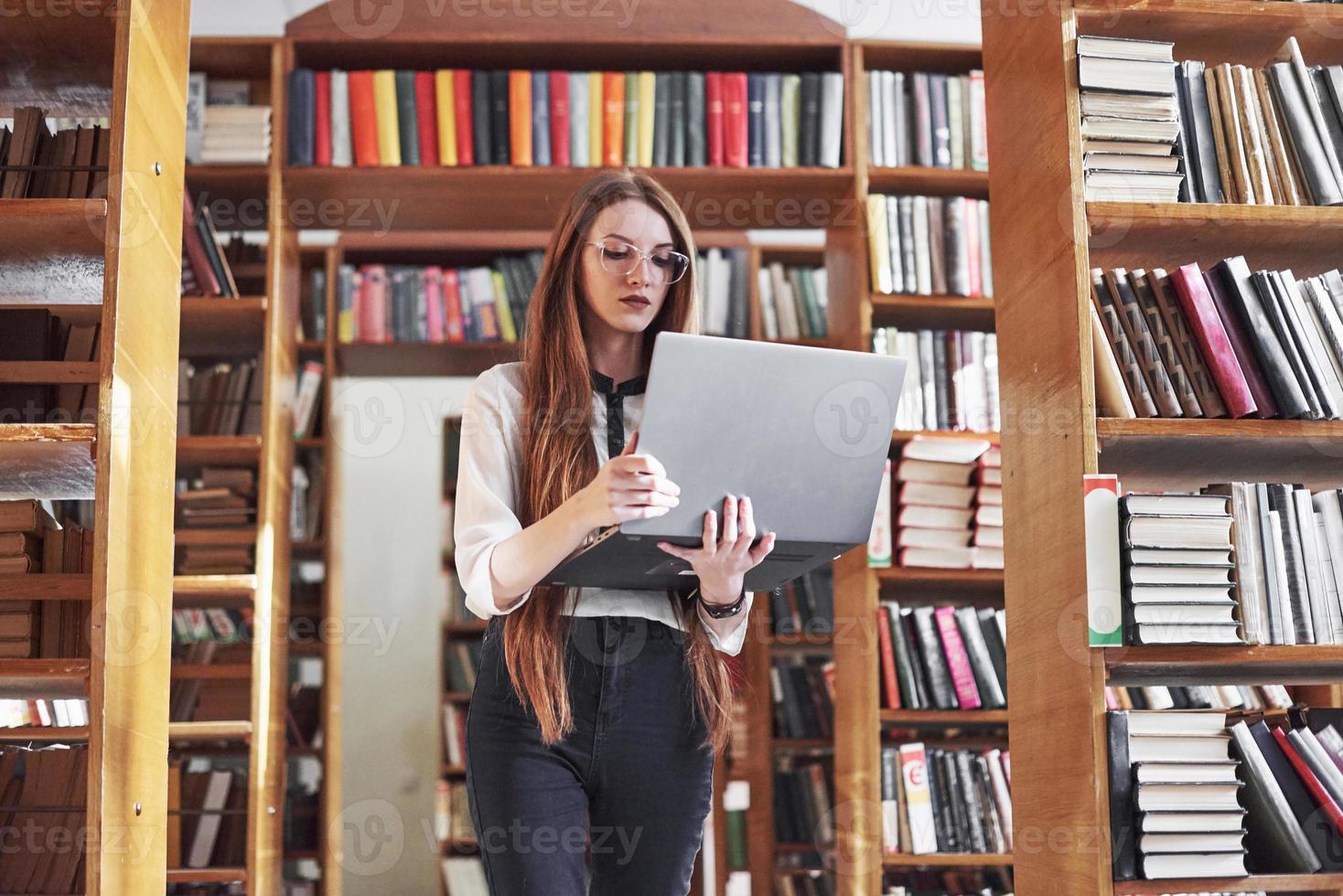 la giovane bella donna è una studentessa in una biblioteca con il suo laptop foto