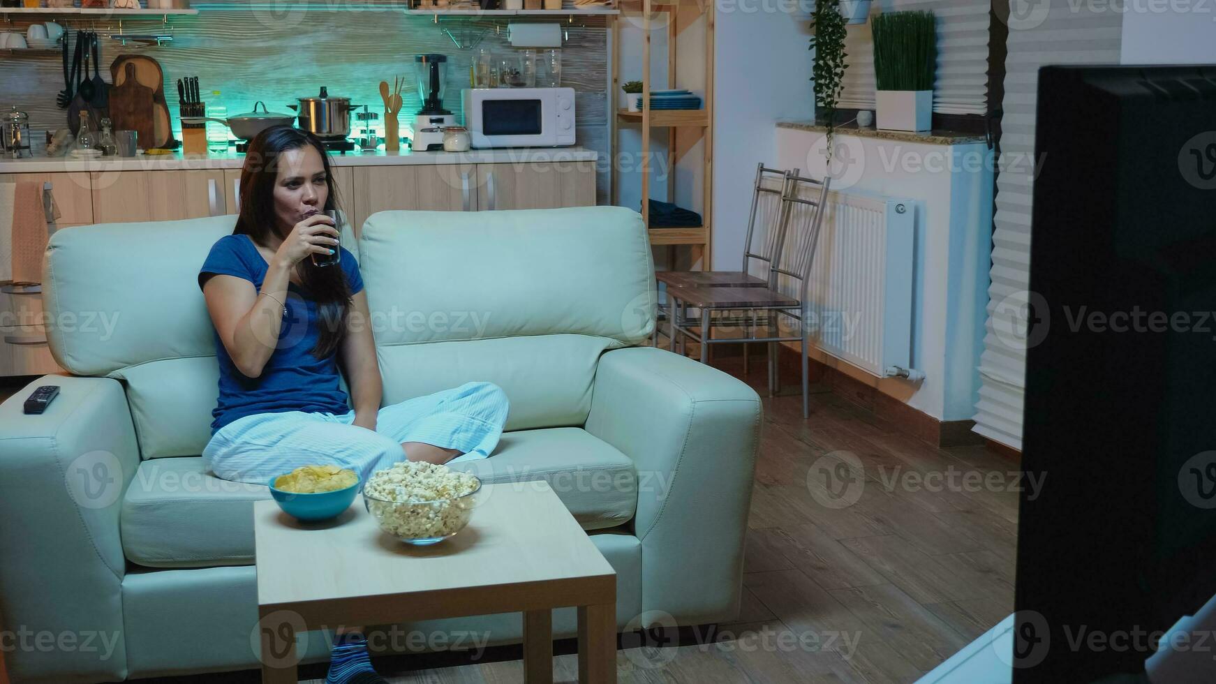 contento donna seduta su divano Guardando film su televisione a casa. emozionato, divertito, solitario signora nel pigiama godendo il sera seduta su confortevole divano nel davanti di televisione mangiare Popcorn. foto