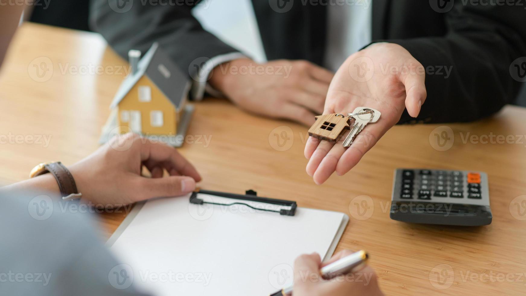 inquadratura ritagliata della firma di un contratto per l'acquisto di una casa mentre il broker tiene la chiave di casa. foto