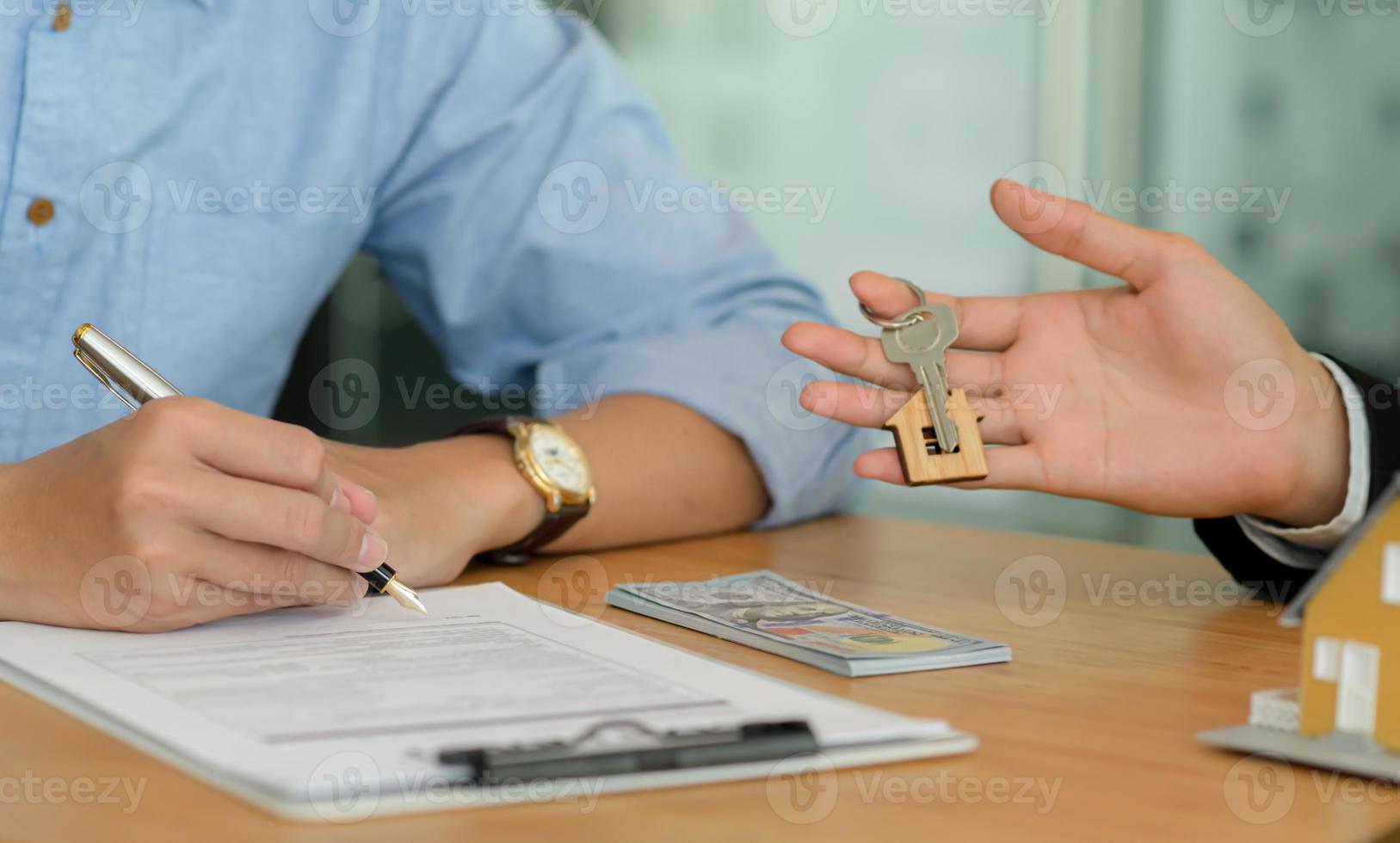 primo piano di acquirenti di case che firmano contratti per la casa e broker di casa che tengono la chiave di casa. foto