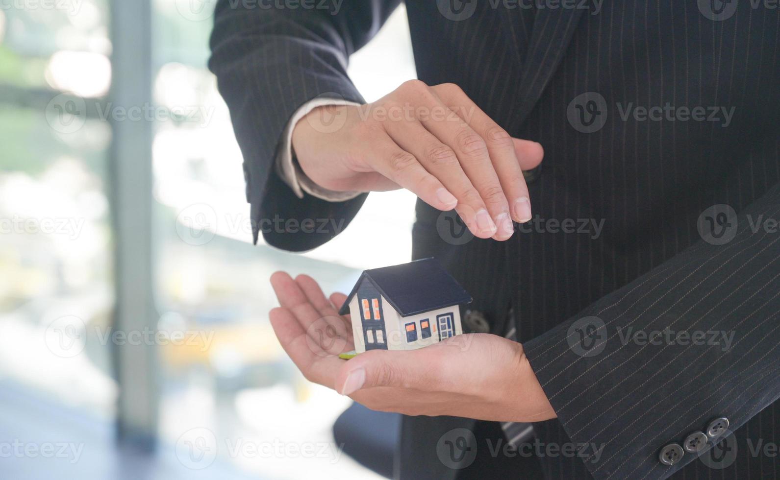 l'agente di assicurazione tiene in mano un modello di casa che mostra il simbolo dell'assicurazione sulla casa. foto