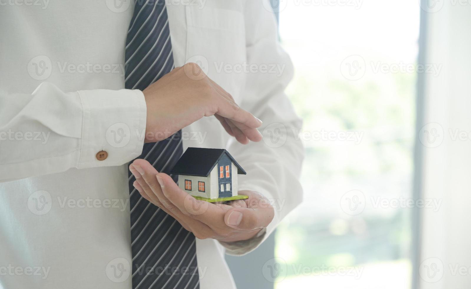 l'agente di assicurazione tiene in mano un modello di casa che mostra il simbolo dell'assicurazione sulla casa. foto