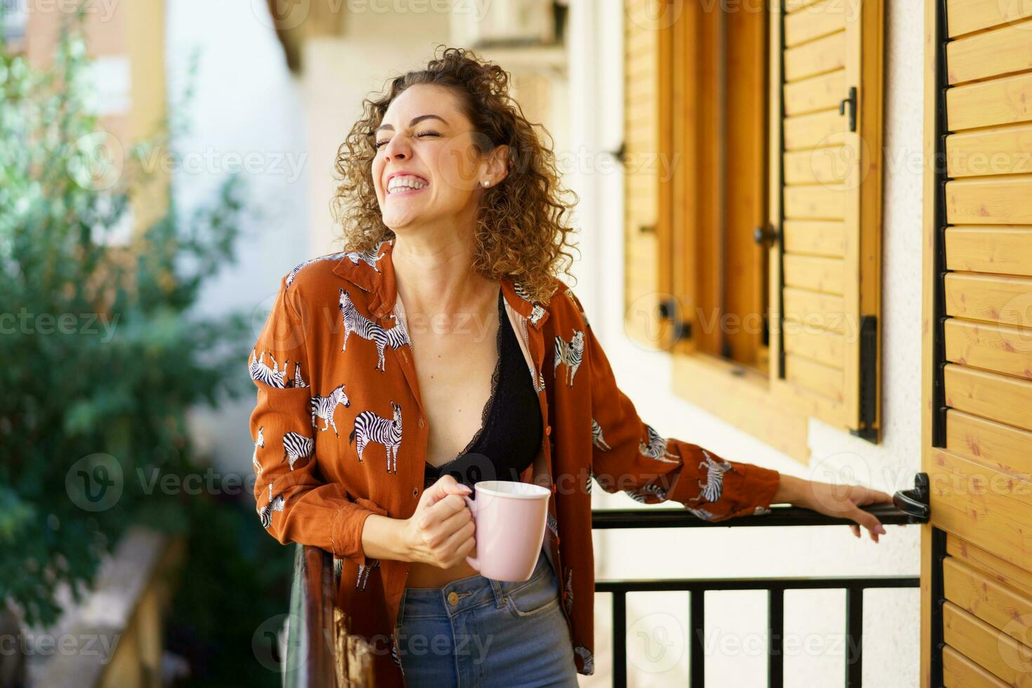 allegro giovane donna Tenere caffè tazza nel mano mentre pendente su balcone di foto