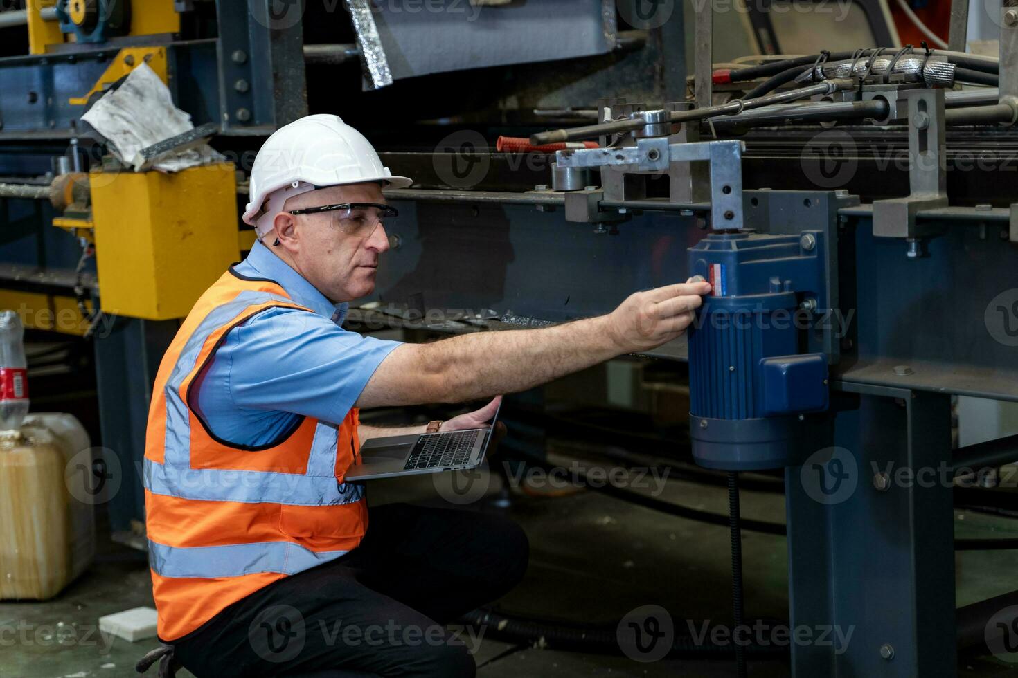 caucasico industriale lavoratore è utilizzando il computer portatile computer per calibrare macchina mentre ispezionando dentro il metallo foglio zincato tetto fabbrica per sicurezza industria foto