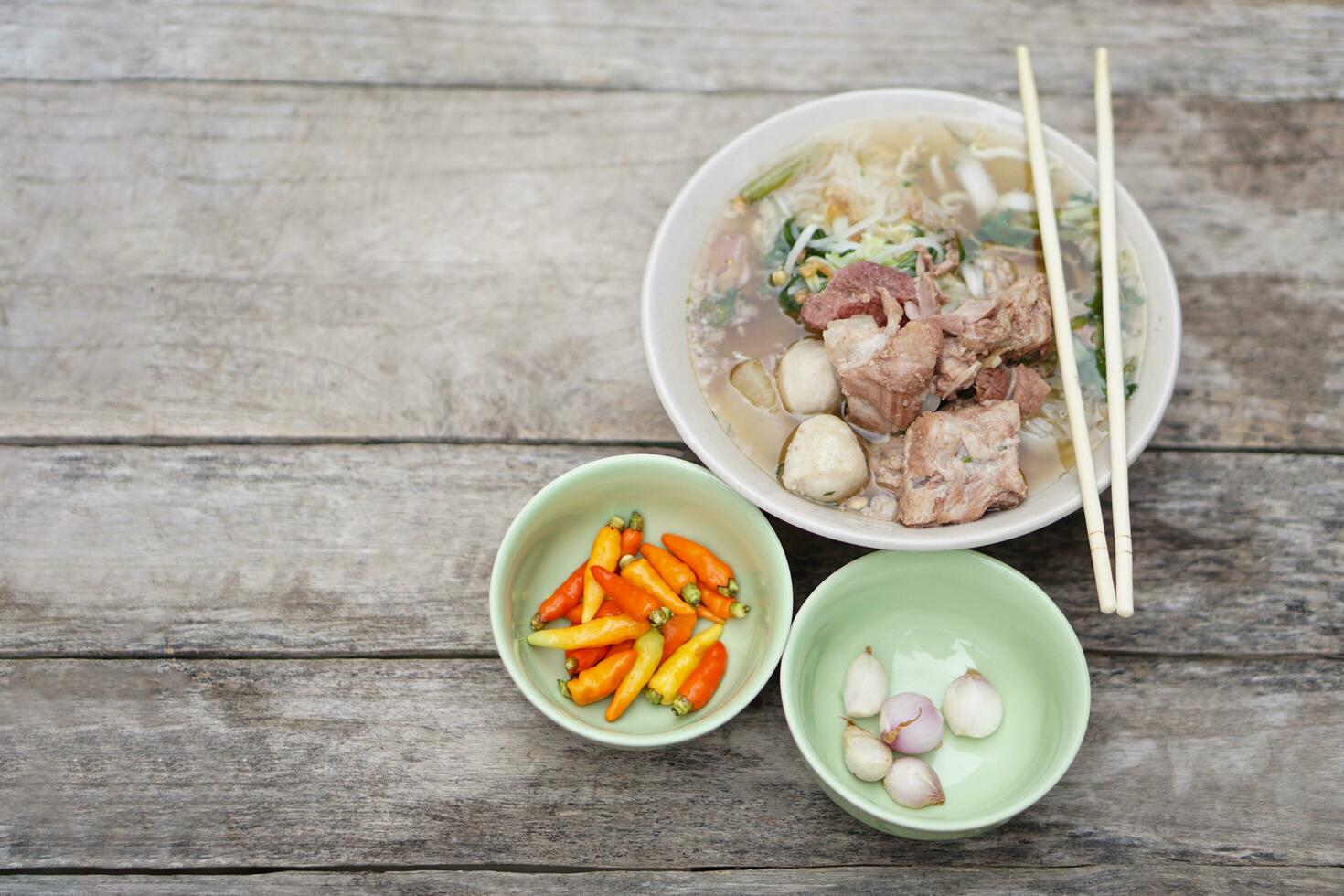 in umido Maiale la minestra con carne palle e verdure nel ciotola, bastoncini su superiore, vecchio di legno sfondo. concetto, tradizionale cibo. preferito menù quello può cucinare o ordine nel spaghetto negozi di alimentari nel Tailandia. foto