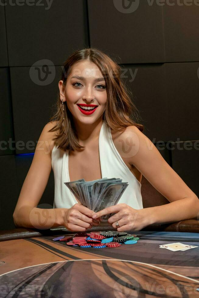 contento giovane donna vincente nel poker, seduta wth banconote a tavolo nel casinò foto