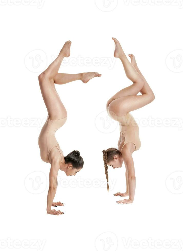 Due flessibile ragazze ginnasti nel beige body l'esecuzione complesso elementi di ginnastica utilizzando sostegno, in posa isolato su bianca sfondo. avvicinamento. foto