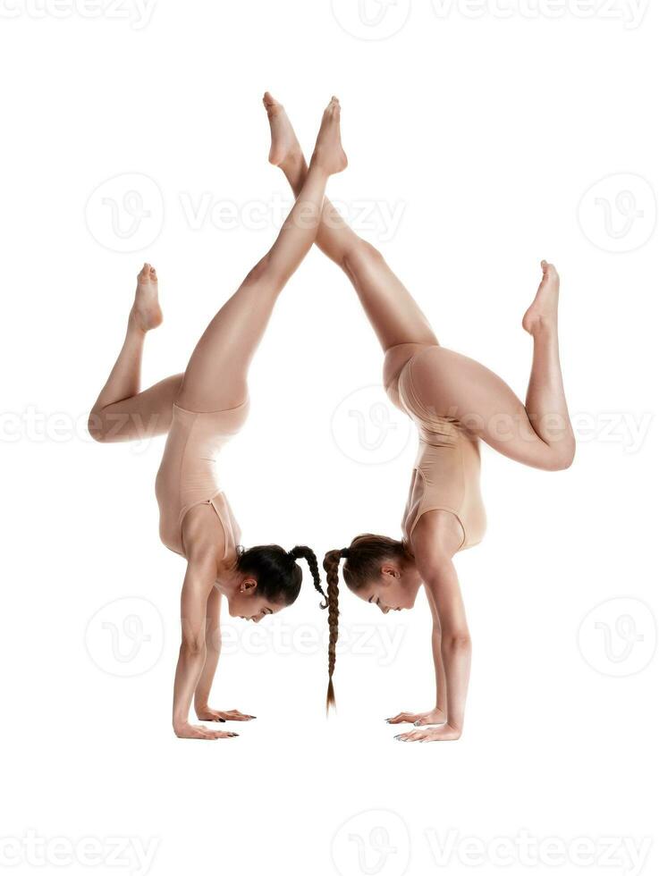 Due flessibile ragazze ginnasti nel beige body siamo l'esecuzione esercizi sottosopra giù utilizzando supporto e in posa isolato su bianca sfondo. avvicinamento. foto
