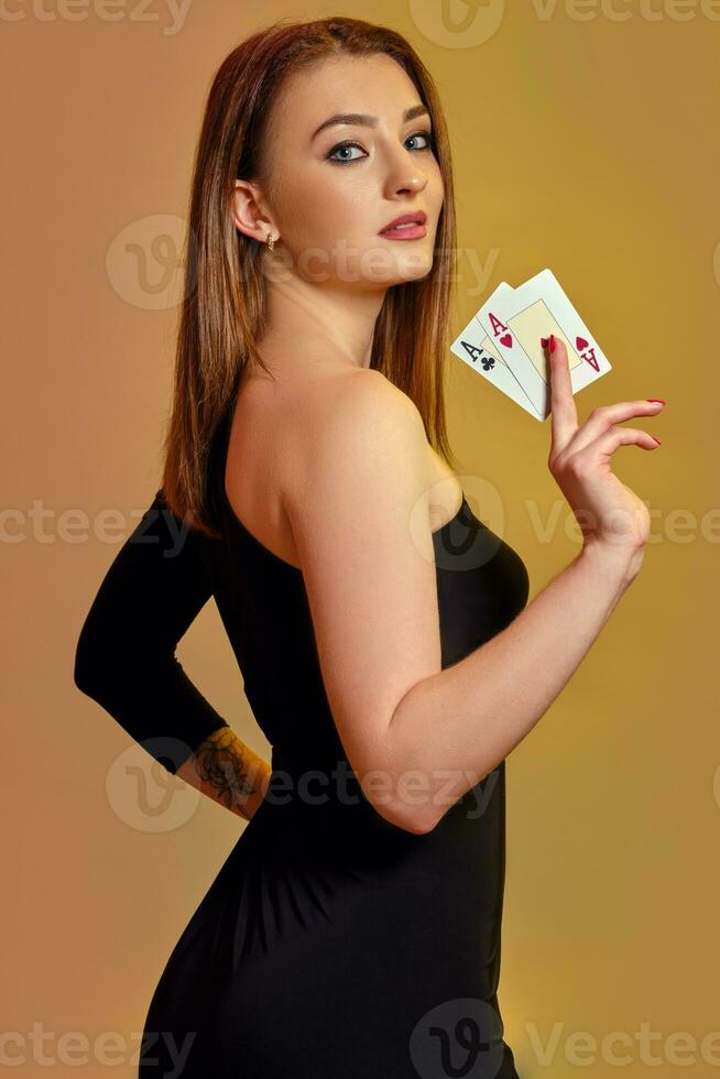 bionda femmina con luminosa trucco, nel nero vestito è mostrando Due assi, in posa lateralmente contro colorato sfondo. gioco d'azzardo, poker, casinò. avvicinamento. foto