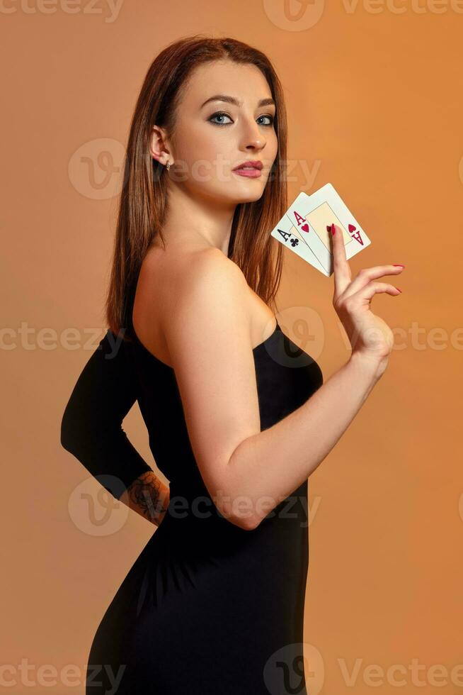 bionda ragazza con luminosa trucco, nel nero vestito è mostrando Due assi, in posa lateralmente contro colorato sfondo. gioco d'azzardo, poker, casinò. avvicinamento. foto