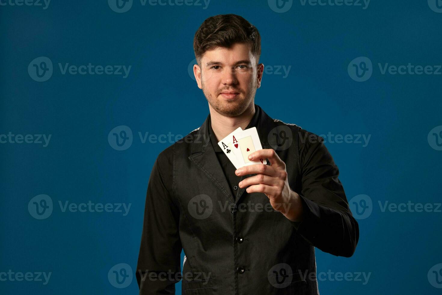 novizio nel poker, nel nero veste e camicia. Tenere Due giocando carte mentre in posa contro blu studio sfondo. gioco d'azzardo, casinò. avvicinamento. foto