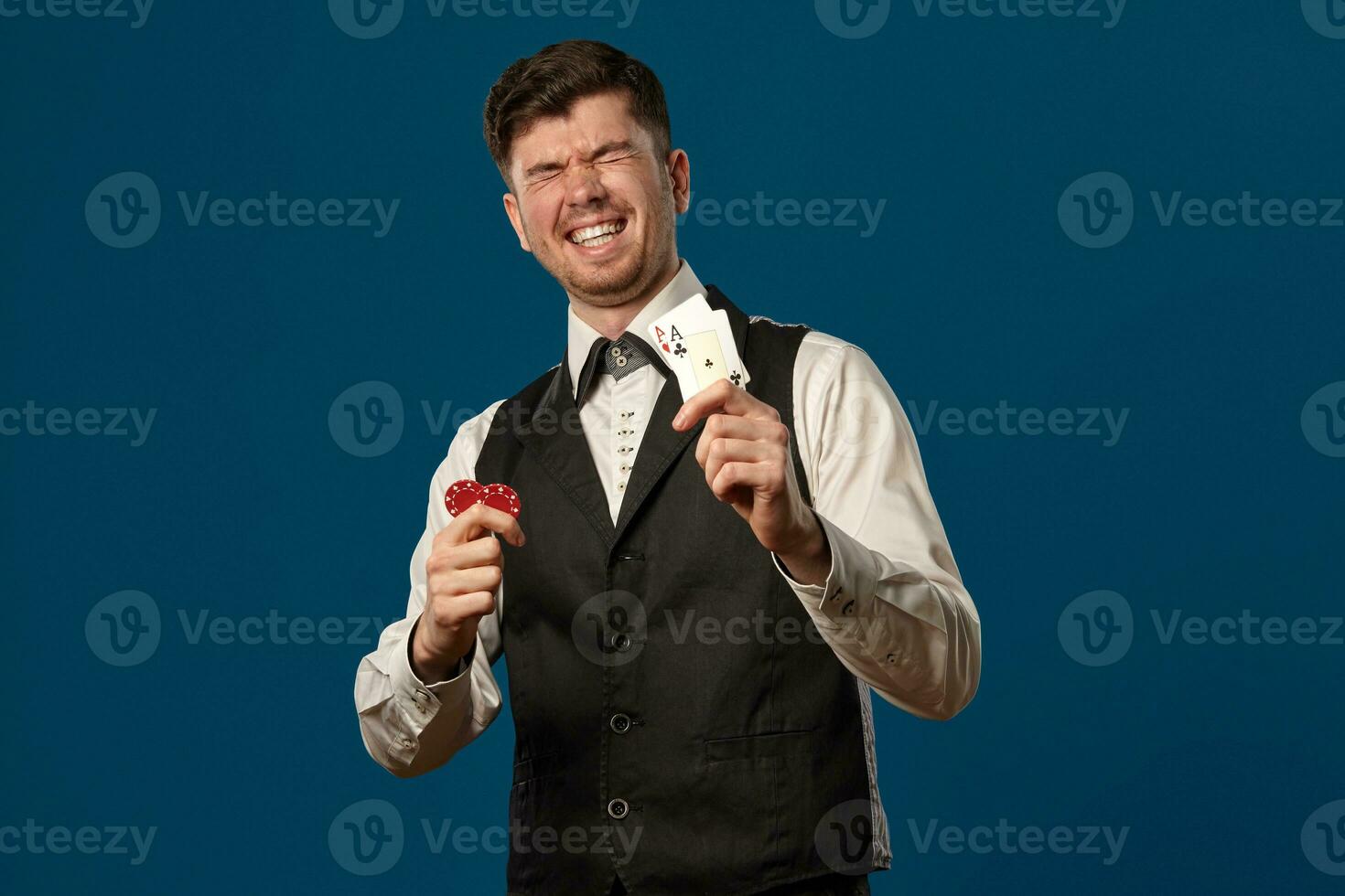 novizio nel poker, nel nero veste e bianca camicia. Tenere Due rosso patatine fritte e assi. in posa contro blu sfondo. gioco d'azzardo, casinò. avvicinamento. foto