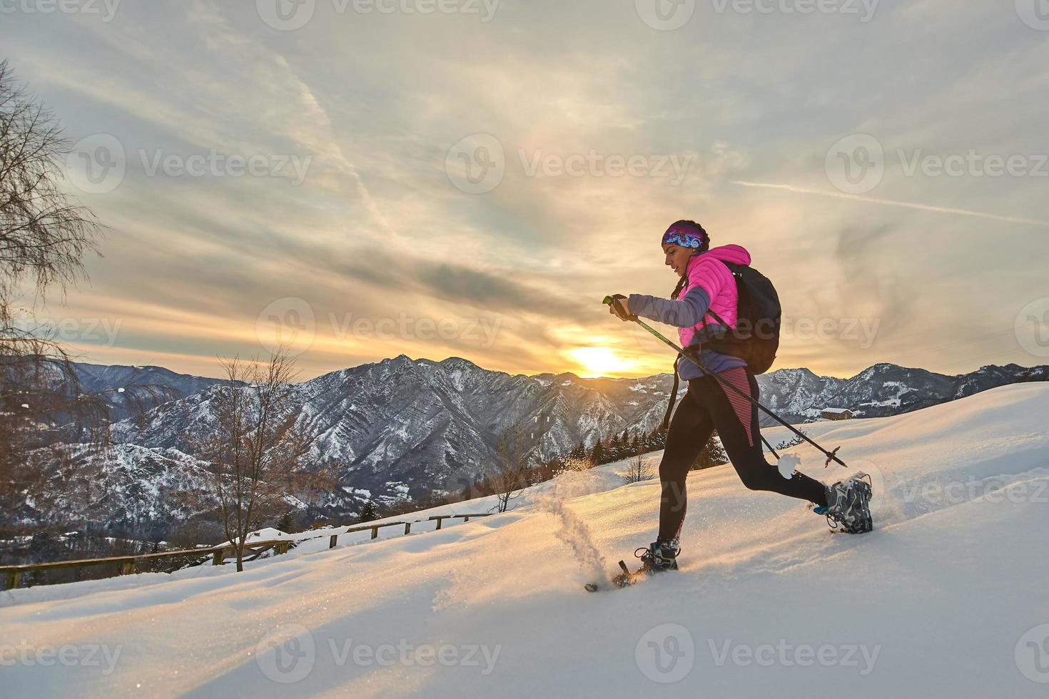 giovane donna sportiva in discesa sulla neve con le racchette da neve in un paesaggio al tramonto foto